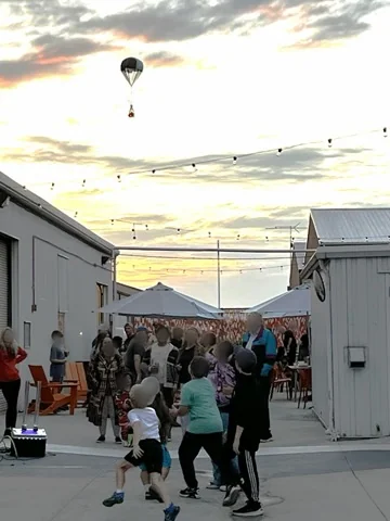 A parachuted gift bag drifting down over a crowd at dusk
